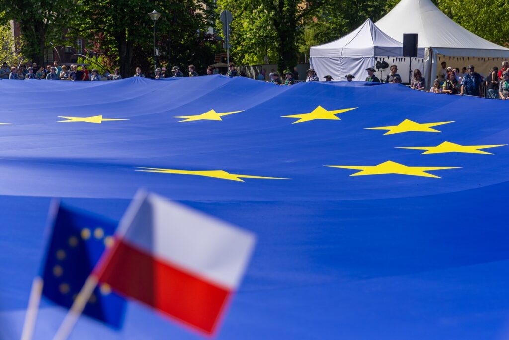 Flagi Polski oraz Unii Europejskiej na tle fragmentu rozłożonej poziomo wielkiej flagi trzymanej przez ludzi, fot. Andrzej Goiński/UMWKP