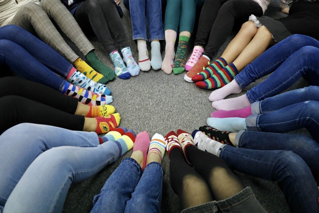 Zdjęcie nóg ułożonych w kręgu ze stopami skierowanymi do środka ubranymi w różnorodne kolorowe skarpety